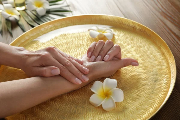 Mujer empapando sus manos en tazón con agua y flores en la mesa, primer plano. Tratamiento de spa —  Fotos de Stock