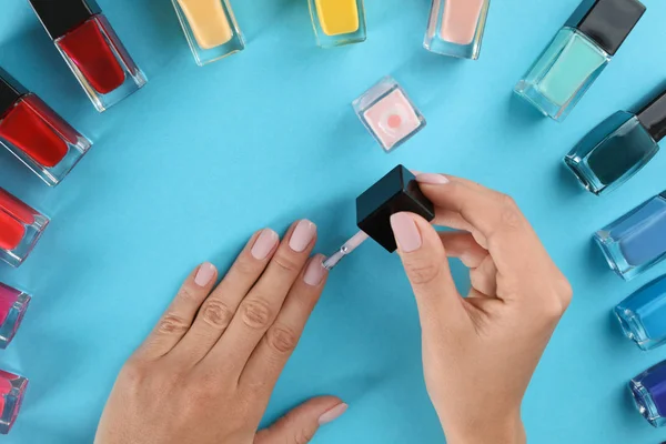 Mujer aplicando esmalte de uñas sobre fondo de color, vista superior — Foto de Stock