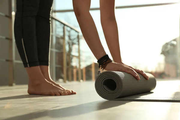 Jeune femme roulant tapis de yoga dans la chambre ensoleillée, gros plan — Photo