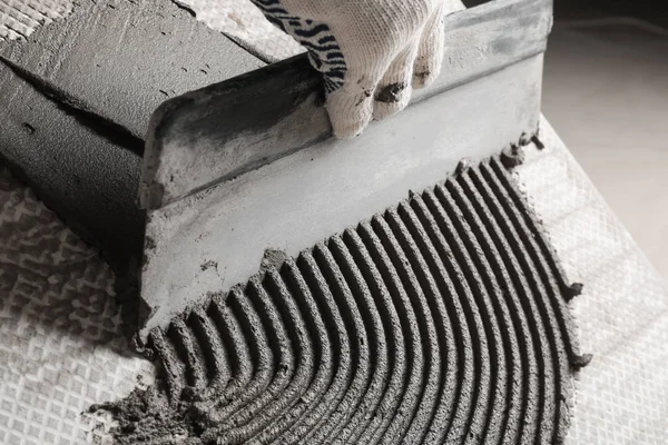 Werknemer het verspreiden van beton op keramische tegels met spatel, close-up — Stockfoto