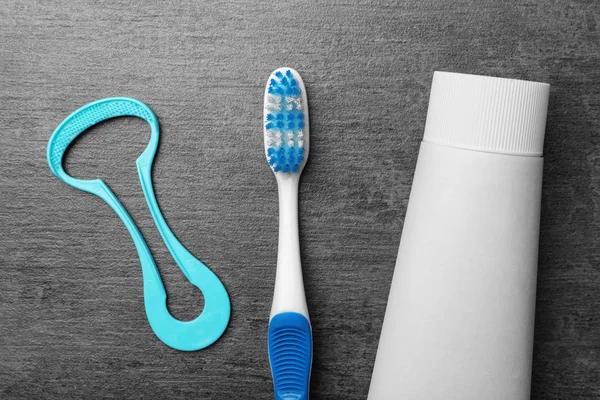 Tongue cleaner, tooth paste and brush on grey background, flat lay