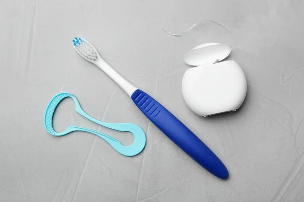 Tongue cleaner, dental floss and toothbrush on grey background, flat lay — Stock Photo, Image