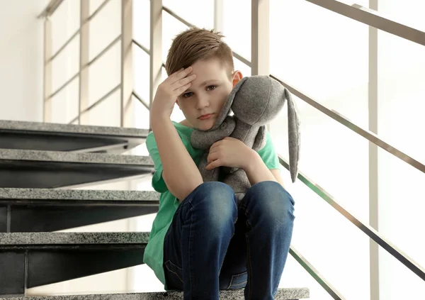 Triste petit garçon avec jouet assis sur les escaliers à l'intérieur — Photo