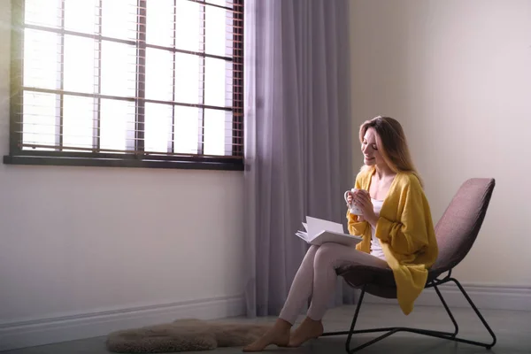Evde güneşlikleri olan pencerenin yanında kitap okuyan genç bir kadın. Metin için alan — Stok fotoğraf