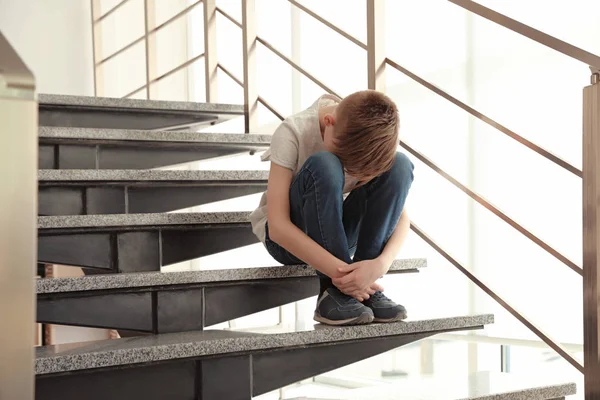 Ledsen liten pojke sitter på trappan inomhus — Stockfoto