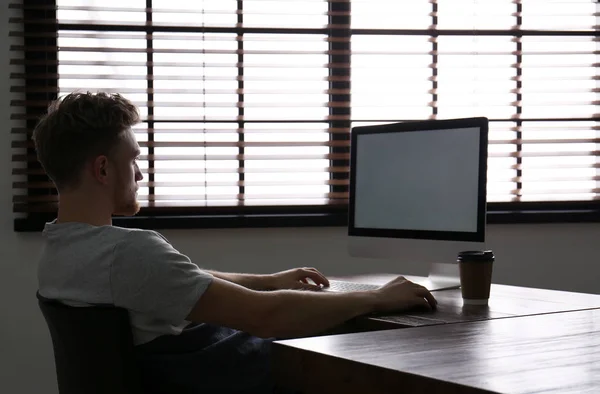 Lonely man sitting at computer with empty screen indoors