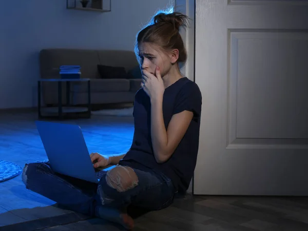 Menina adolescente aterrorizada com laptop no chão no quarto escuro. Perigo da internet — Fotografia de Stock