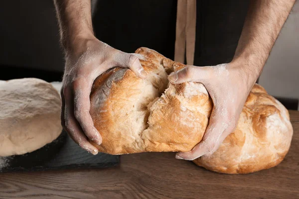 Masculino padeiro segurando pão sobre mesa, close-up — Fotografia de Stock