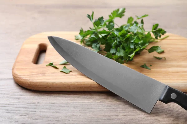 Tabla de cortar con cuchillo de chef y perejil fresco sobre mesa de madera — Foto de Stock