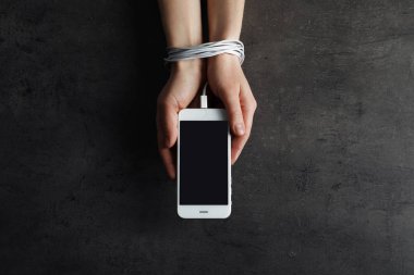 Cep telefonunu elinde tutan kadın, gri arka planda şarj kablosuyla bağlanmış, yukarıda. Yalnızlık kavramı