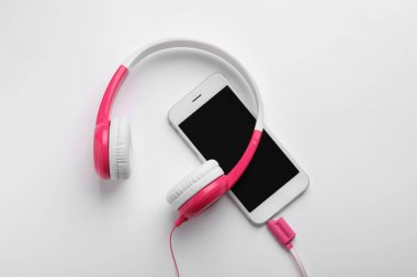 Beyaz arka planda şık kulaklıklar ve modern telefon, üst görünüm