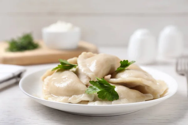 Plate of tasty cooked dumplings served on white wooden table