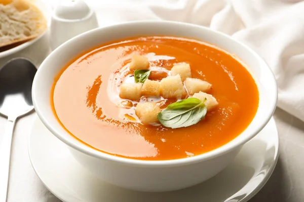 Bowl of sweet potato soup with croutons and basil served on table, closeup
