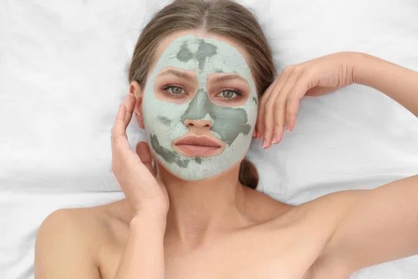 Beautiful woman with clay facial mask on white fabric, above view — Stock Photo, Image