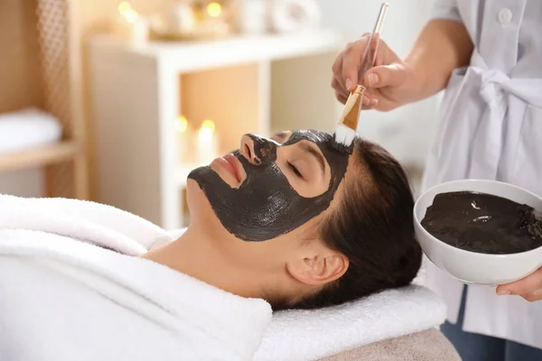 Kosmetologis menerapkan topeng hitam ke wajah wanita di spa salon — Stok Foto