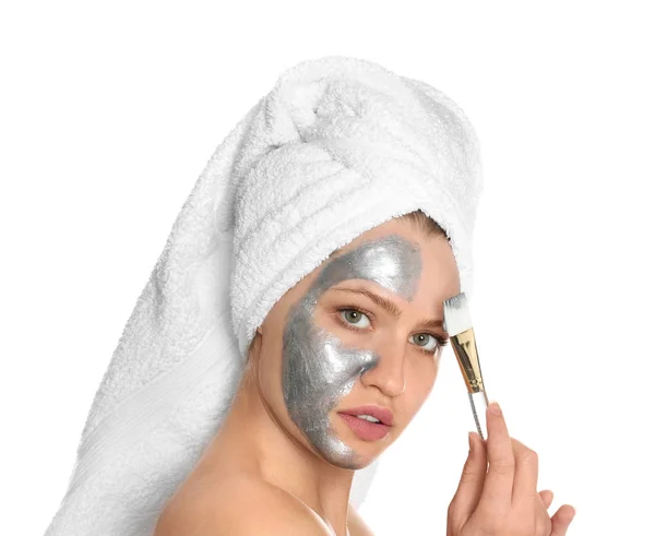 Mooie vrouw het toepassen van zilveren masker op haar gezicht tegen witte achtergrond — Stockfoto