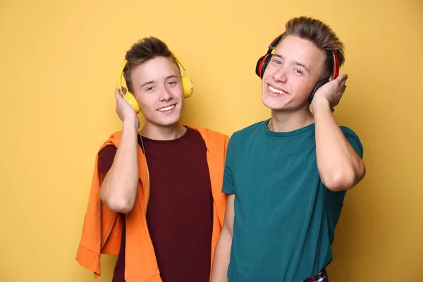 Teenager-Zwillingsbrüder mit Kopfhörern auf farbigem Hintergrund — Stockfoto