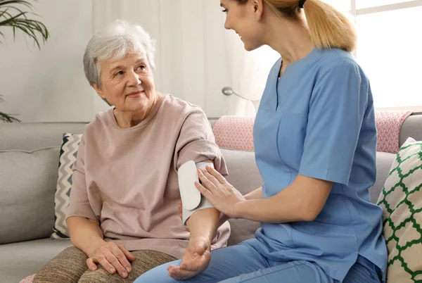 Enfermera midiendo la presión arterial de una anciana en el interior. Asistencia a personas mayores — Foto de Stock