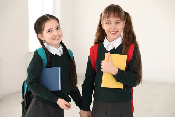 Retrato de meninas bonitos em uniforme escolar com mochilas e livros dentro de casa — Fotografia de Stock