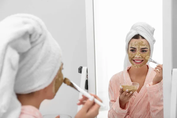 Mladá žena, která používá hliněnou masku na obličeji nedaleko zrcadla v koupelně. Péče o pokožku — Stock fotografie