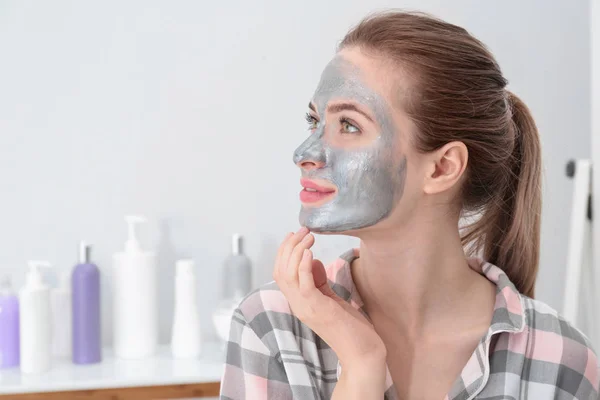 Młoda kobieta z maski oczyszczającej na twarzy w łazience, miejsce na tekst. Pielęgnacja skóry — Zdjęcie stockowe