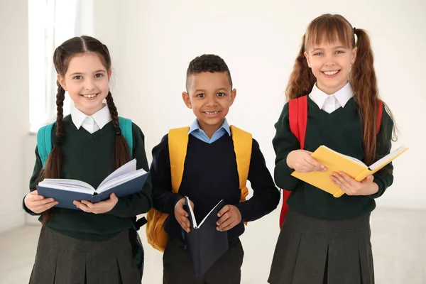 Πορτρέτο των χαριτωμένα παιδιά σε σχολική στολή με σακίδια και βιβλία σε εσωτερικούς χώρους — Φωτογραφία Αρχείου