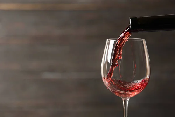 Despejando vinho tinto em vidro de garrafa contra fundo de madeira borrada, close-up. Espaço para texto — Fotografia de Stock
