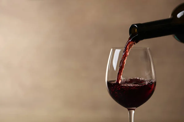 Pouring red wine into glass from bottle against blurred beige background, closeup. Space for text — Stock Photo, Image