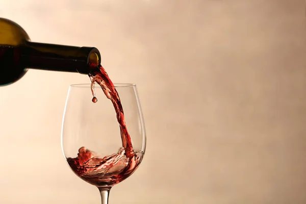 Pouring red wine into glass from bottle against blurred beige background, closeup. Space for text — Stock Photo, Image