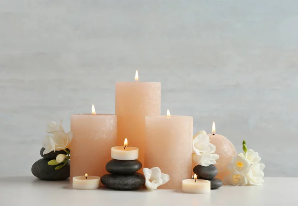 Schöne Komposition mit Kerzen, Steinen und Blumen auf dem Tisch vor hellem Hintergrund — Stockfoto