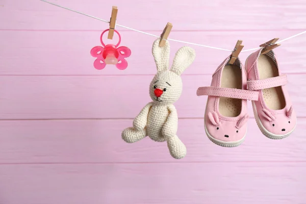 Coppia di scarpe, ciuccio e coniglietto giocattolo sulla linea di lavanderia sullo sfondo in legno. Accessori per bambini — Foto Stock