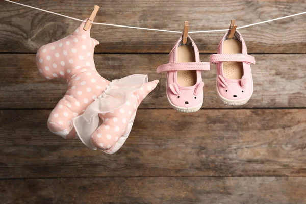 Cão de brinquedo e par de sapatos na linha de lavanderia contra fundo de madeira. Acessórios para bebés — Fotografia de Stock