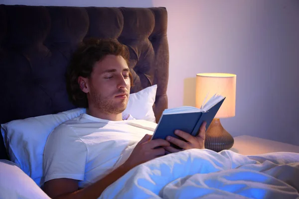 Красивый молодой человек читает книги в темной комнате ночью. Время спать — стоковое фото