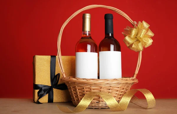 Botellas de vino en canasta de mimbre con lazo y regalo sobre mesa sobre fondo de color — Foto de Stock