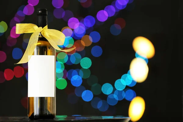 Bottle of wine with bow-knot on table against blurred lights, space for text. Bokeh effect