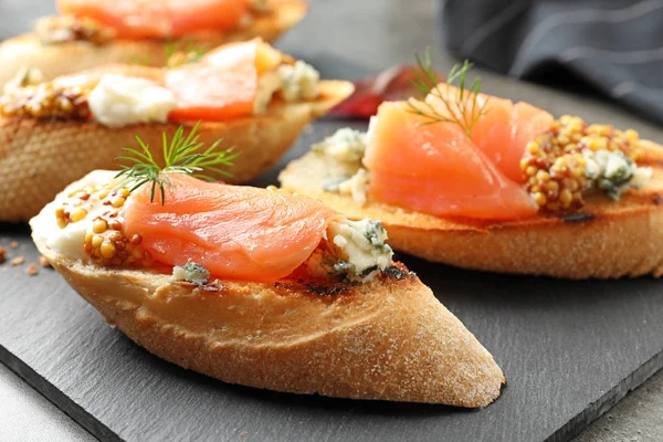 Sabrosos bruschettas con salmón y queso azul en plato de pizarra, primer plano —  Fotos de Stock