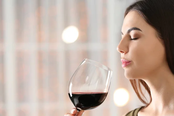 Beautiful young woman with glass of luxury red wine indoors, closeup view. Space for text