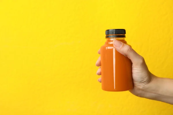 Femme tenant bouteille de jus de carotte sur fond de couleur, gros plan avec de l'espace pour le texte — Photo