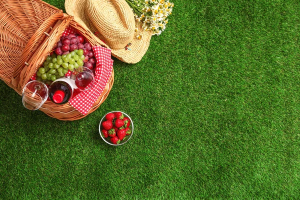 Composição de leigos planos com cesta de piquenique, vinho e frutas na grama, espaço para texto — Fotografia de Stock