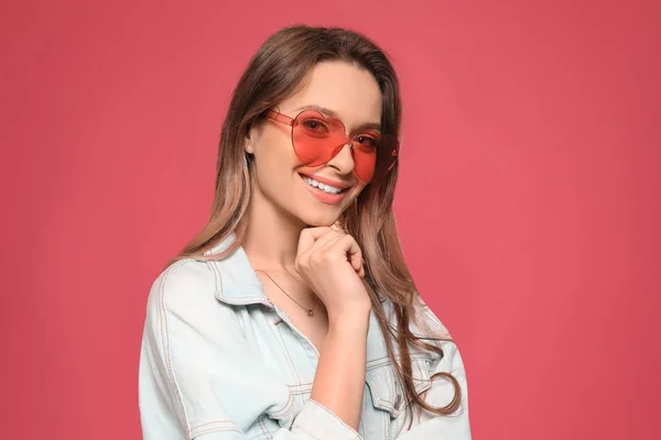 Retrato de una hermosa mujer joven con gafas de sol en forma de corazón sobre fondo de color — Foto de Stock