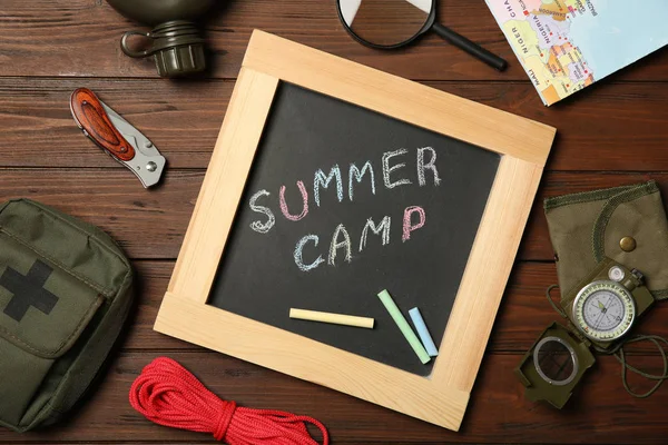 Крейдяна дошка з текстом SUMMER CAMP та кемпінгове обладнання на дерев'яному фоні, плоска покладена — стокове фото