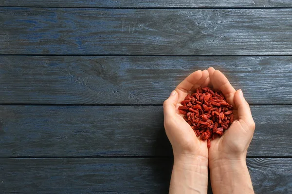 Donna che tiene bacche di goji secche rosse su sfondo blu di legno, vista dall'alto. Spazio per testo — Foto Stock