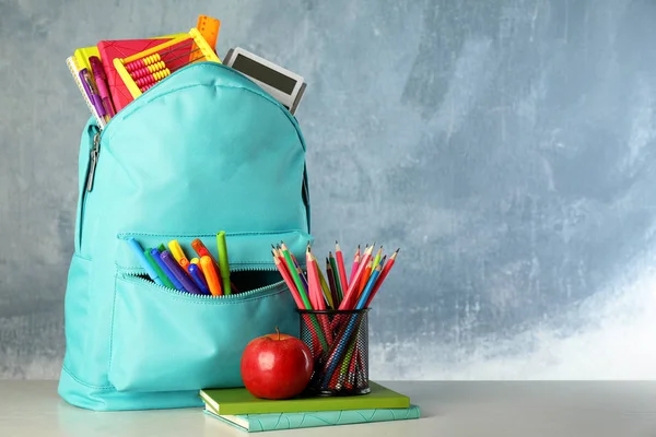 Mochila brillante con papelería escolar sobre la mesa sobre fondo azul, espacio para texto —  Fotos de Stock