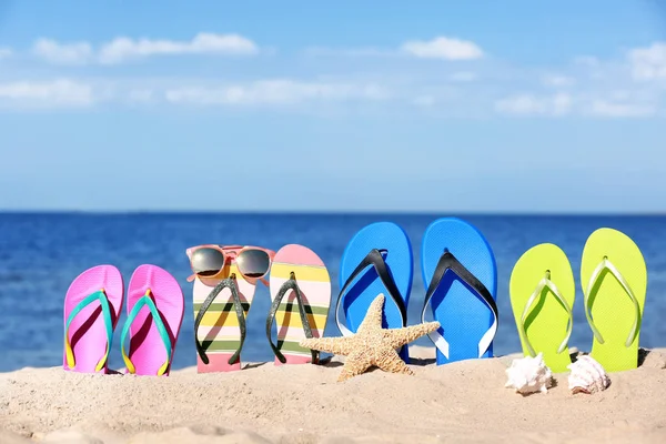 Composizione con infradito luminose sulla sabbia vicino al mare in estate. Accessori da spiaggia — Foto Stock