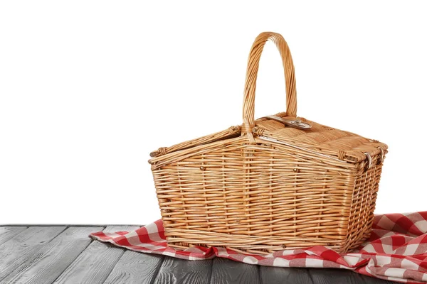 Closed wicker picnic basket with checkered tablecloth on wooden table against white background — Stock Photo, Image