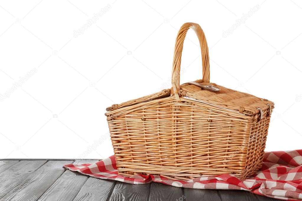 Closed wicker picnic basket with checkered tablecloth on wooden table against white background