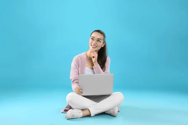 Giovane donna in abito casual con computer portatile seduto su sfondo di colore — Foto Stock