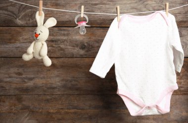 Bodysuit, emzik ve ahşap arka plan karşı çamaşır hattı üzerinde oyuncak tavşan. Bebek aksesuarları