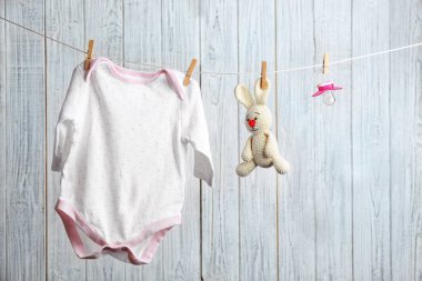 Bodysuit, emzik ve ahşap arka plan karşı çamaşır hattı üzerinde oyuncak tavşan. Bebek aksesuarları