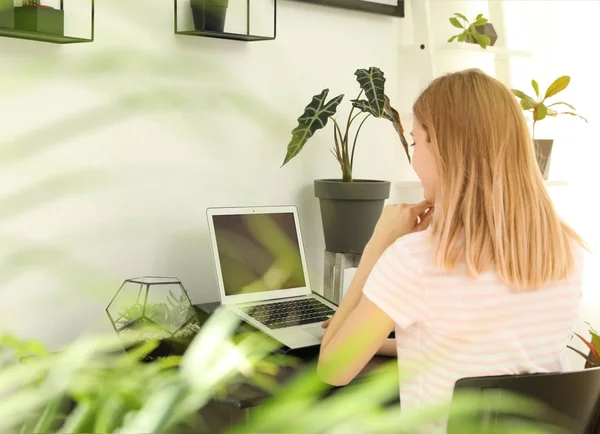 Mladá žena, která používá přenosný počítač doma, místo pro text. Interiér v módní místnosti s rostlinami — Stock fotografie